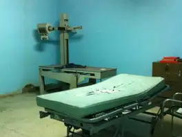 Sala de rayos X de un hospital, con el falso techo roto y una camilla con el colchón rasgado.