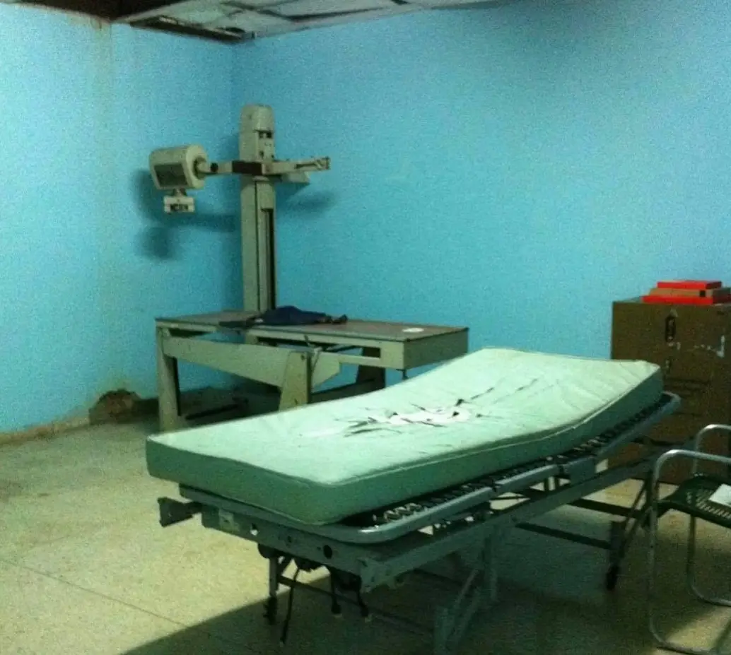 Sala de rayos X de un hospital, con el falso techo roto y una camilla con el colchón rasgado.
