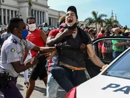 Un policía y hombres de civil sujetan a un joven que grita junto a una patrulla, durante una protesta frente al Capitolio de La Habana.