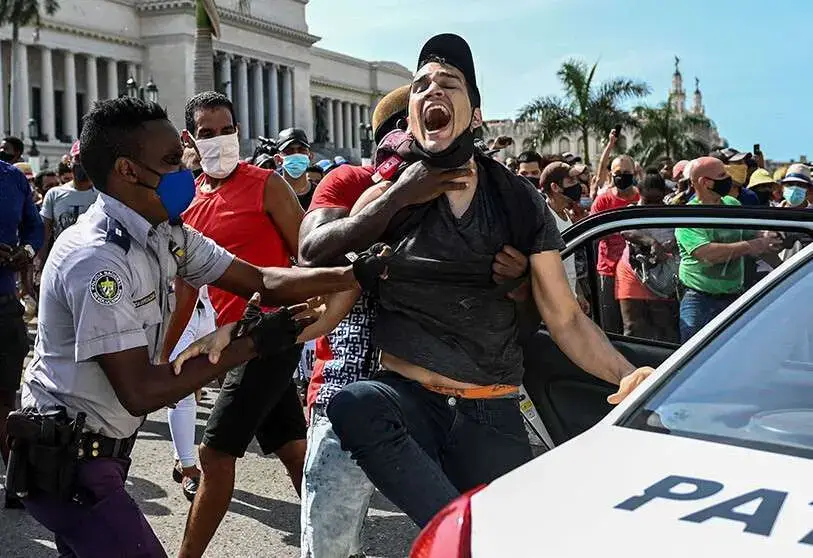 Un policía y hombres de civil sujetan a un joven que grita junto a una patrulla, durante una protesta frente al Capitolio de La Habana.